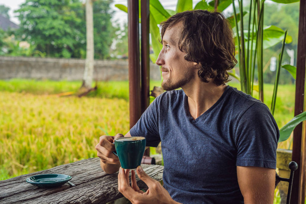 Man with a cup of coffee on the cafe veranda near the rice terraces on Bali, Indonesia - Φωτογραφία, εικόνα