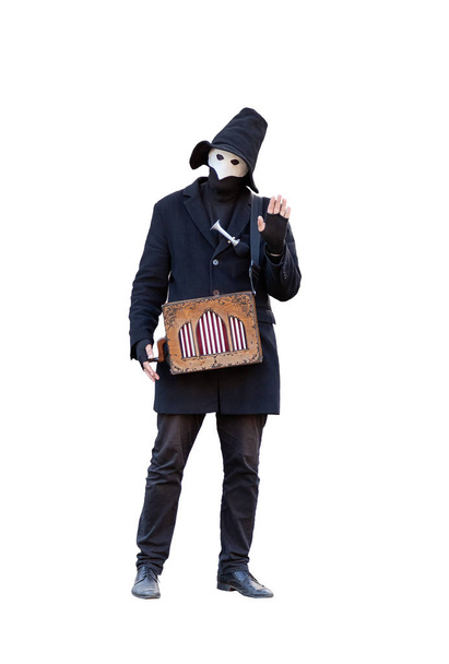 ein Straßenmusiker mit Drehleier in der Maske in schwarzer Kleidung mit schwarzem Hut auf weißem Hintergrund winkt - Foto, Bild