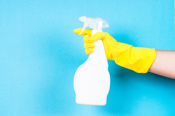 Ręka w rękawice żółty trzymać czyszczenia butelka agenta na niebieskim tle. - Zdjęcie, obraz