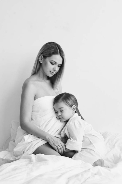 Красивые беременные мама и дочь играют на белой кровати в
  - Фото, изображение