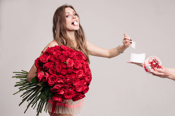 Красивая леди с красными розами берет конфетку из коробки
. - Фото, изображение