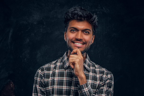 Handsome Indian guy in plaid shirt smiling and looks at the camera with a piercing look. - Photo, Image