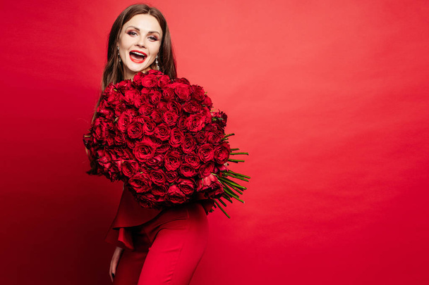 Prachtige vrouw in rode jurk houden boeket rozen - Foto, afbeelding