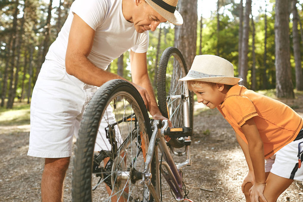 Isä ja poika korjaavat polkupyörää puistossa.
.  - Valokuva, kuva