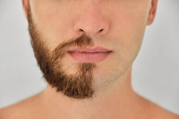 Half shaved. A young man with beard on half of the face on light grey background. Close up. - Foto, Imagen