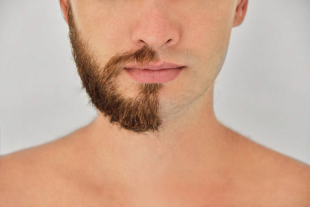 Half shaved. A young man with beard on half of the face on light grey background. Close up. - Foto, imagen