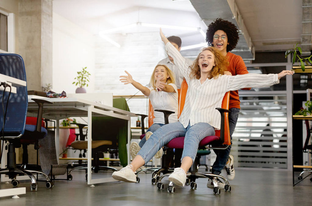 Молоді веселі ділові люди змагаються на офісних стільцях і посміхаються
 - Фото, зображення
