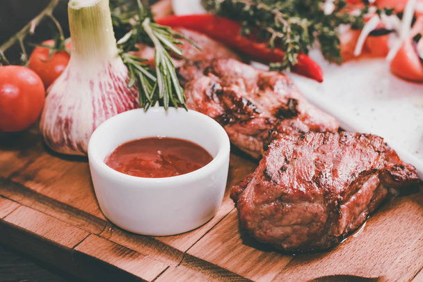 Close-up van geroosterde varkensvlees hals met kruiden, groenten en ketchup op houten bord - Foto, afbeelding