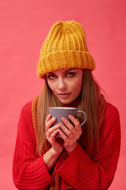 Beautiful teenage girl in warm cozy sweater with cup of hot drink. Red background. Studio - Foto, immagini