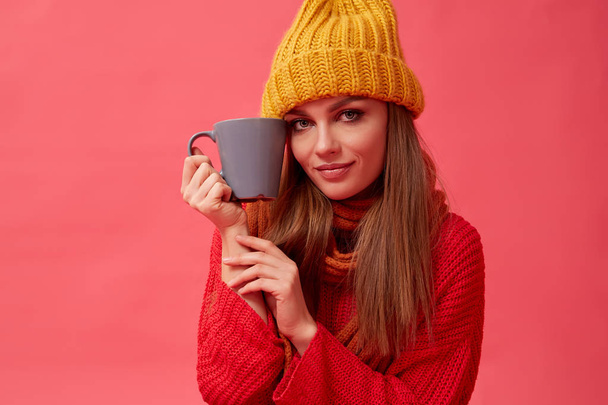 Beautiful teenage girl in warm cozy sweater with cup of hot drink. Red background. Studio - 写真・画像