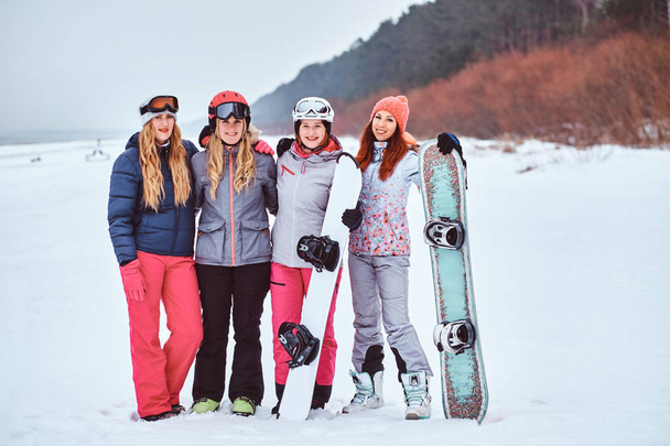 Весёлые подруги в спортивной зимней одежде со сноубордами и позирующими лыжами
  - Фото, изображение