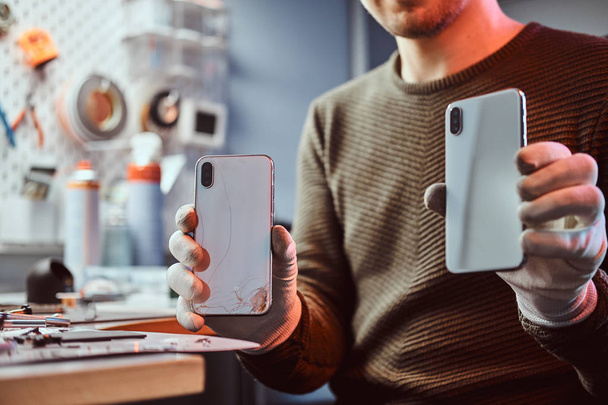 Techniker hält zwei identische Smartphones zum Vergleich, in einer Hand kaputt und in einer anderen neu - Foto, Bild