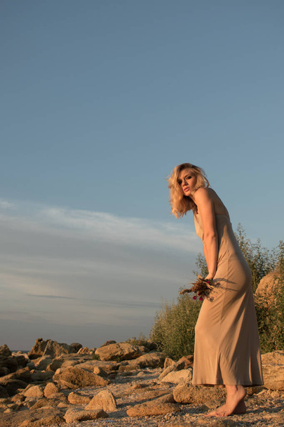 fashion woman  in long dress with dry flowers in hands on a beach, casual blonde with smokey eyes and beautiful body - 写真・画像