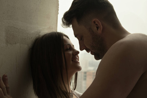 Schönes romantisches Paar vor dem Hintergrund eines großen hellen Fensters. attraktiver Mann kuschelt Brünette im Hemd  - Foto, Bild