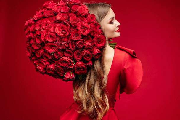 Hermosa joven morena en rojo con racimo de rosas rojas en el hombro
. - Foto, Imagen