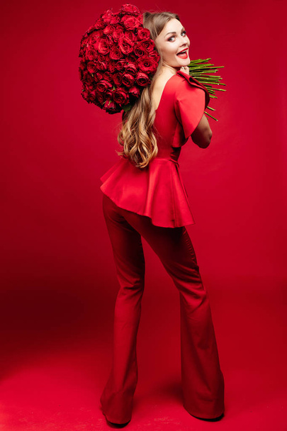 Eerlijke haired elegante vrouw in rode kleding houden van bloemen. - Foto, afbeelding