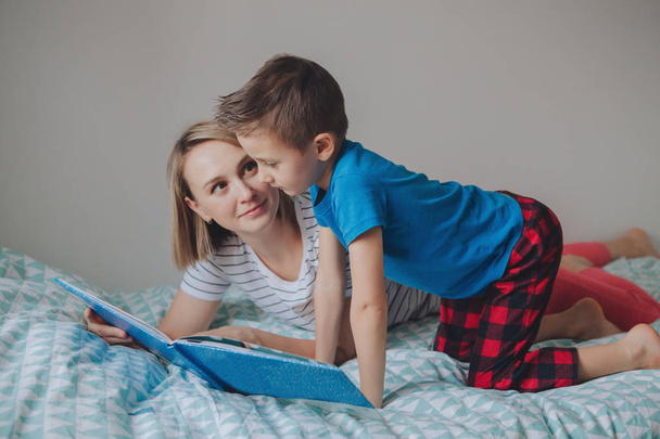 Сім'я з двох людей сидить на ліжку в книзі для читання спальні. Мати і син вдома проводять час разом. Батьки спілкуються з дитиною. Справжні люди спосіб життя
  - Фото, зображення
