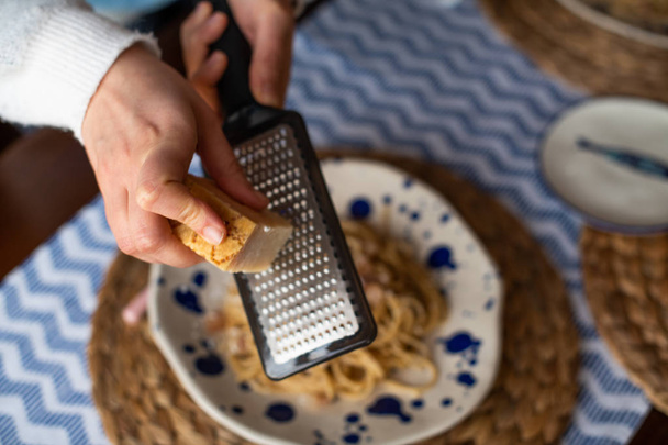 mulher mãos ralando queijo parmesão em macarrão carbonara
 - Foto, Imagem