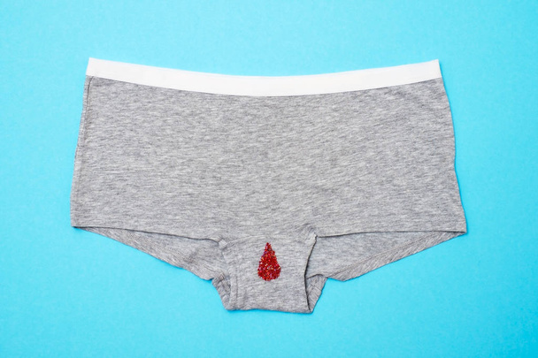 Red drop from beads on pants on blue background. Menstruation period - Foto, imagen