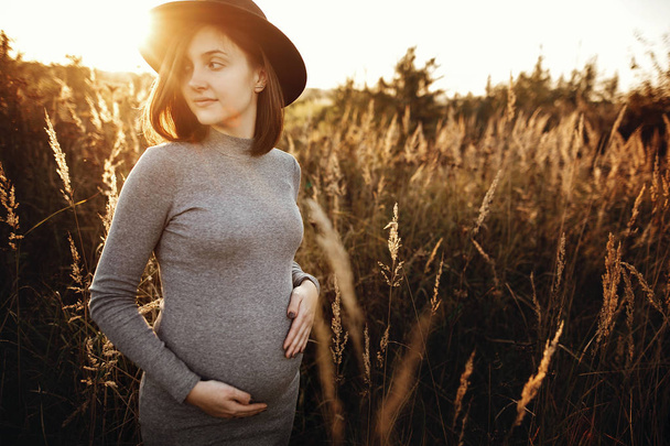 Стильная беременная женщина, держащаяся за живот и расслабляющаяся в суматохе.
 - Фото, изображение