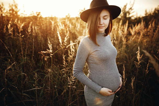 Stylový těhotná žena držící ruce na břicho a relaxaci v su - Fotografie, Obrázek
