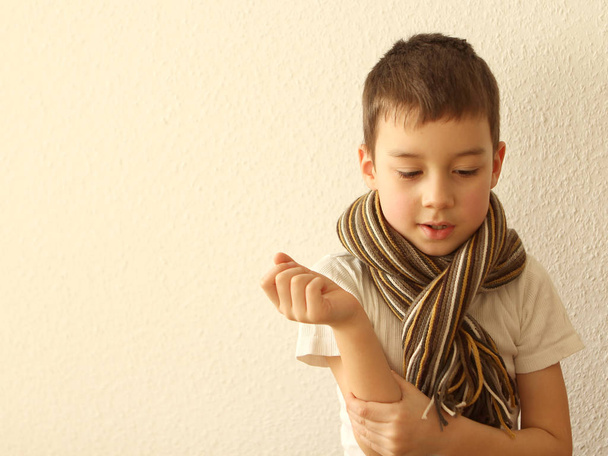 boy in white clothes and a warm striped scarf on a light background close up. - Zdjęcie, obraz