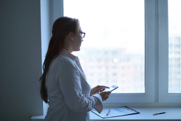 business woman with a smartphone while standing near an office window. - Φωτογραφία, εικόνα