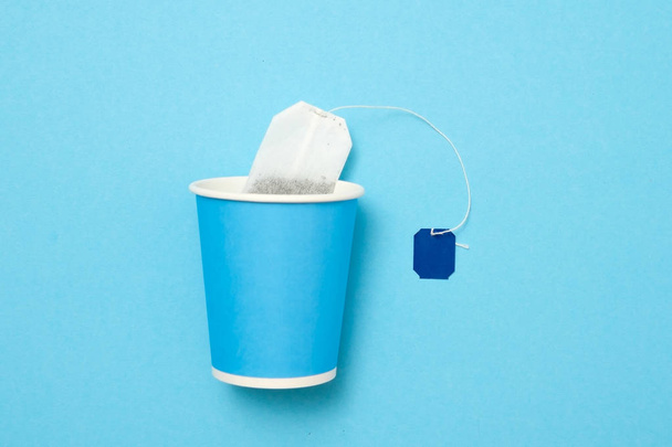 Teabag with empty label with paper mug on blue background. - Photo, Image