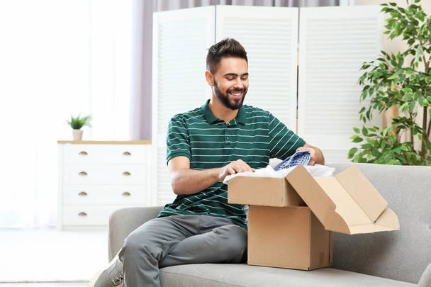 Young man opening parcel on sofa at home - Foto, immagini