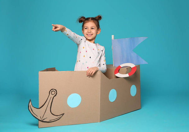 Cute little girl playing with cardboard boat on color background - Foto, imagen