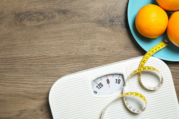 Scales, measuring tape, oranges and space for text on wooden background, top view. Weight loss - 写真・画像