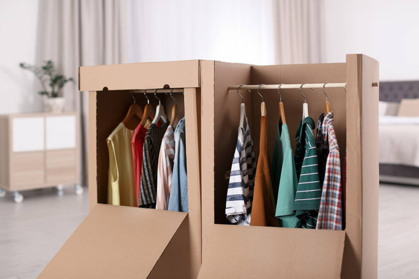 Cardboard wardrobe boxes with clothes on hangers in bedroom - 写真・画像