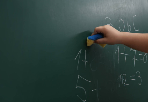 Little child wiping math sums from chalkboard, closeup. Space for text - Zdjęcie, obraz