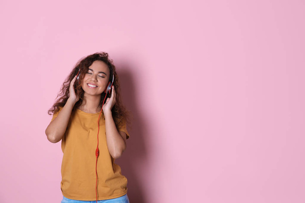 African-American girl listening to music with headphones on color background, space for text - Foto, Imagen