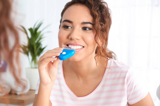 Young African-American woman using teeth whitening device at home - Foto, Imagem