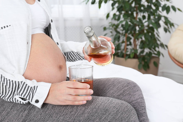Pregnant woman pouring whiskey into glass at home. Alcohol addiction - Foto, immagini