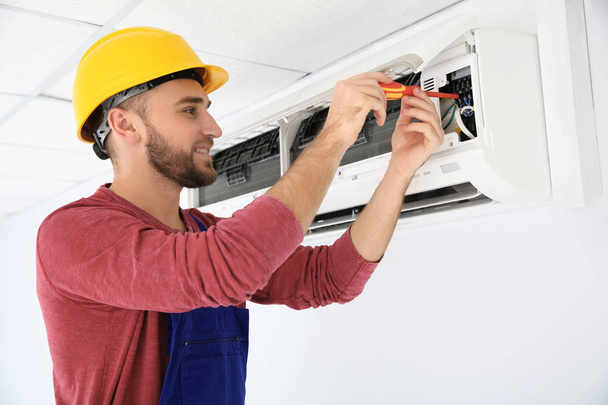 Electrician with screwdriver repairing air conditioner indoors - Foto, Bild