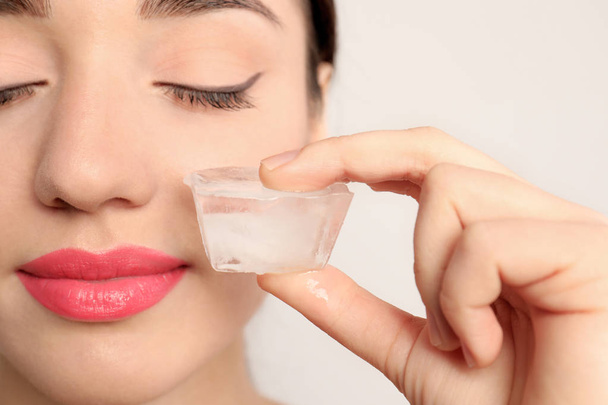 Young woman with ice cube on light background. Skin care - Φωτογραφία, εικόνα