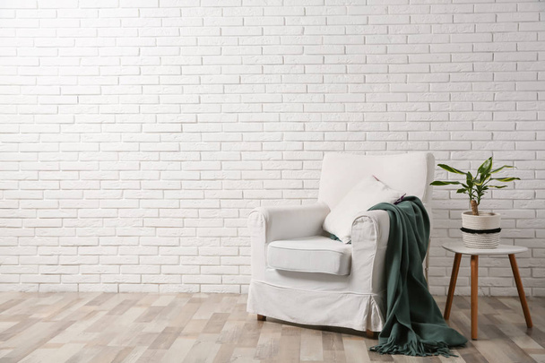 Comfortable armchair near brick wall in modern room interior. Space for text - Φωτογραφία, εικόνα