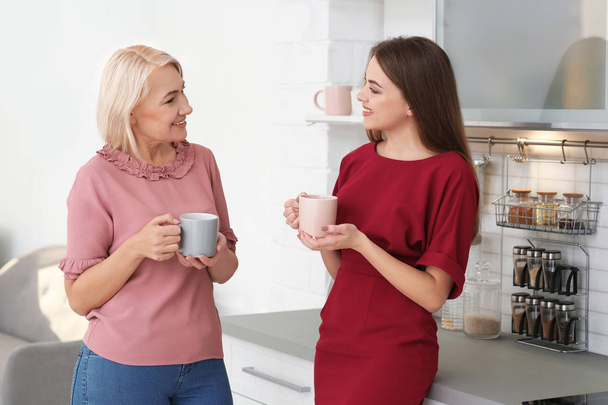 Portrait of mature woman and her daughter drinking tea in kitchen - Foto, imagen