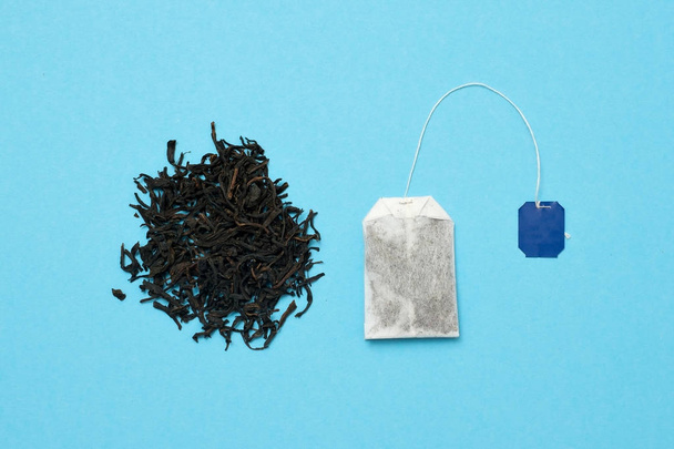 Teebeutel und schwarze Blätter auf blauem Hintergrund. welche Art von Tee ist besser - Foto, Bild
