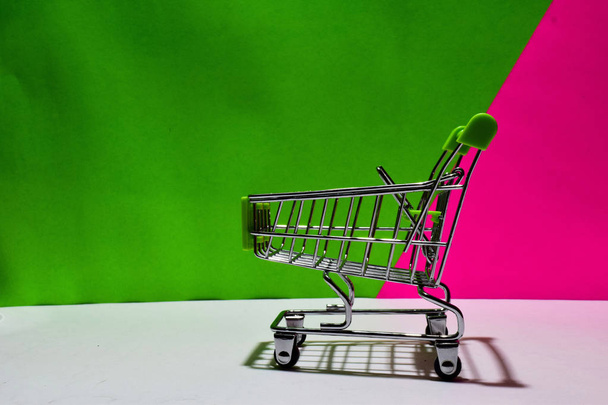 Tyhjä vihreä ostoskärry eristetty vihreä ja vaaleanpunainen tausta. Sähköisen kaupankäynnin ja yritysmarkkinoinnin käsite
 - Valokuva, kuva