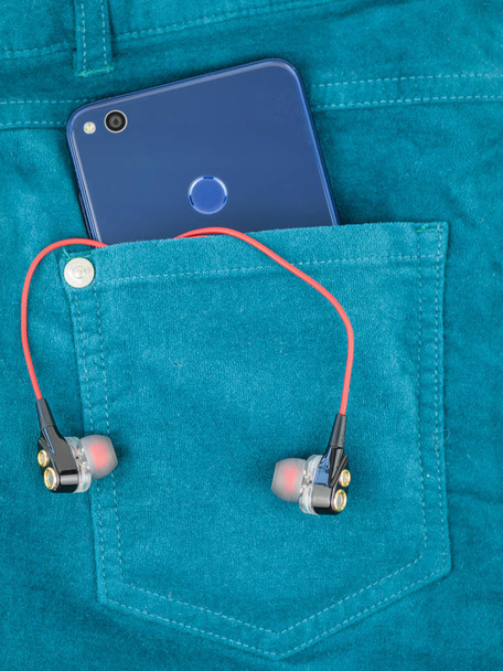 Niebieski telefon jest w kieszeni zielone spodnie jeansowe ze słuchawkami. - Zdjęcie, obraz