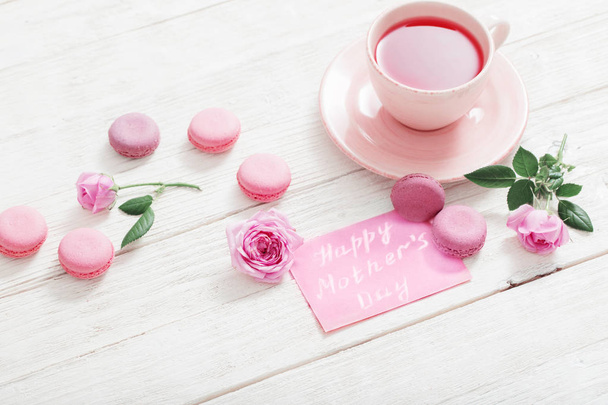 kopje thee en een roze bitterkoekjes op witte houten tafel - Foto, afbeelding