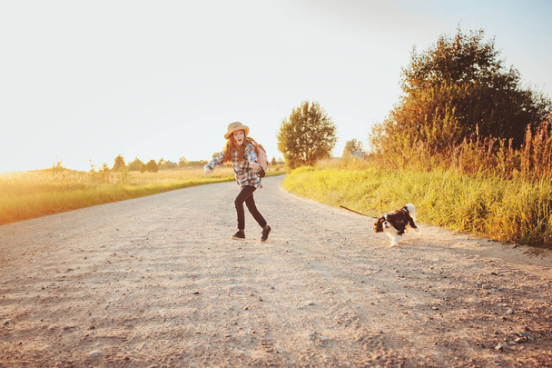 happy child girl enjoying summer vacations with her dog, walking and playing on sunny meadow. Traveling, exploring new places and rural living concept - Zdjęcie, obraz