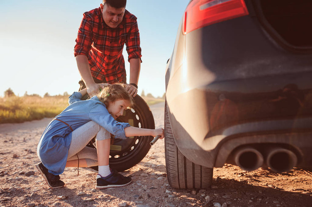 father and daughter changing broken tire during summer rural road trip. Kid helping to fix problems with car - 写真・画像