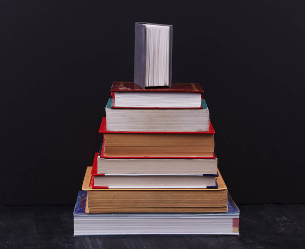 Stack of books on a black background with small book on top - Photo, Image