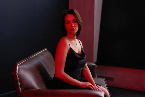  Mooie jonge vrouw poseren in zwarte jurk in studio - Foto, afbeelding