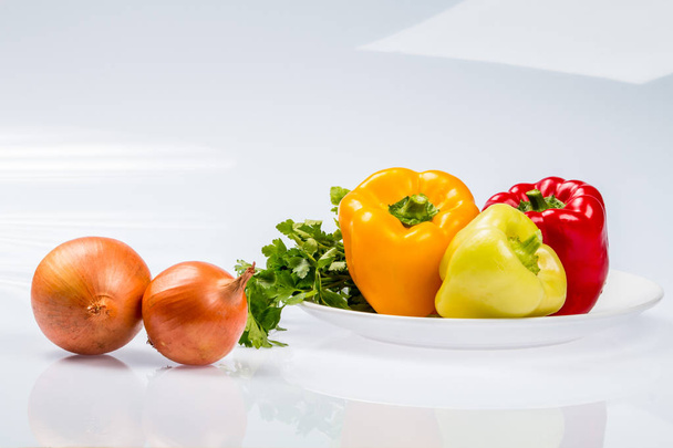 Trois délicieux poivrons bulgares mûrs, citron vert, rouge, orange, et deux oignons dans une assiette, sur un fond blanc
 - Photo, image