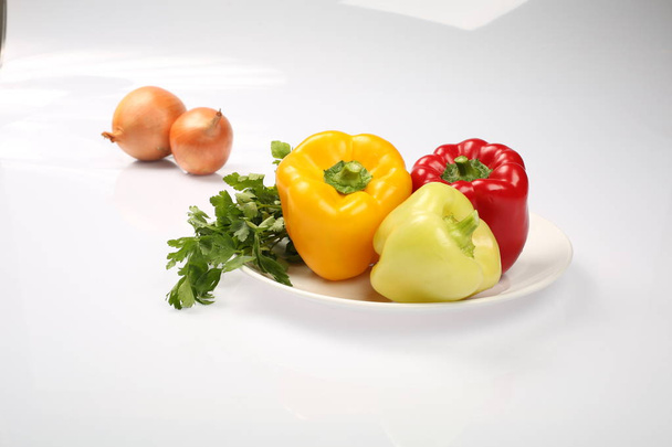 Три вкусных спелых болгарских перца, лайм, красный, оранжевый, и два лука на тарелке, на белом фоне
 - Фото, изображение